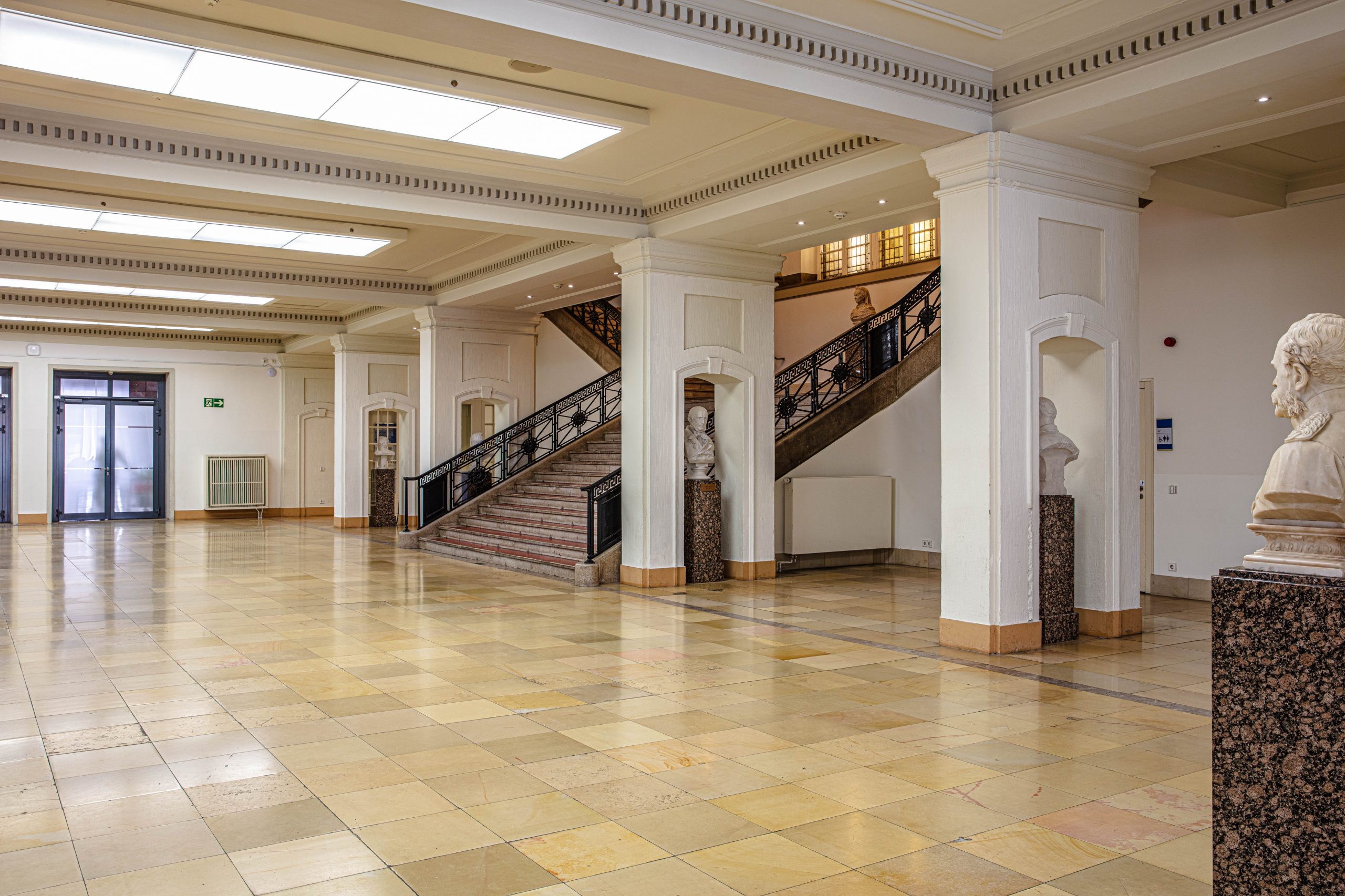 Foyer im Erdgeschoss des LVH Langenbeck Virchow Haus Berlin mit Marmorboden, Treppenaufgang und historischen Skulpturen als Empfangsbereich für Veranstaltungen