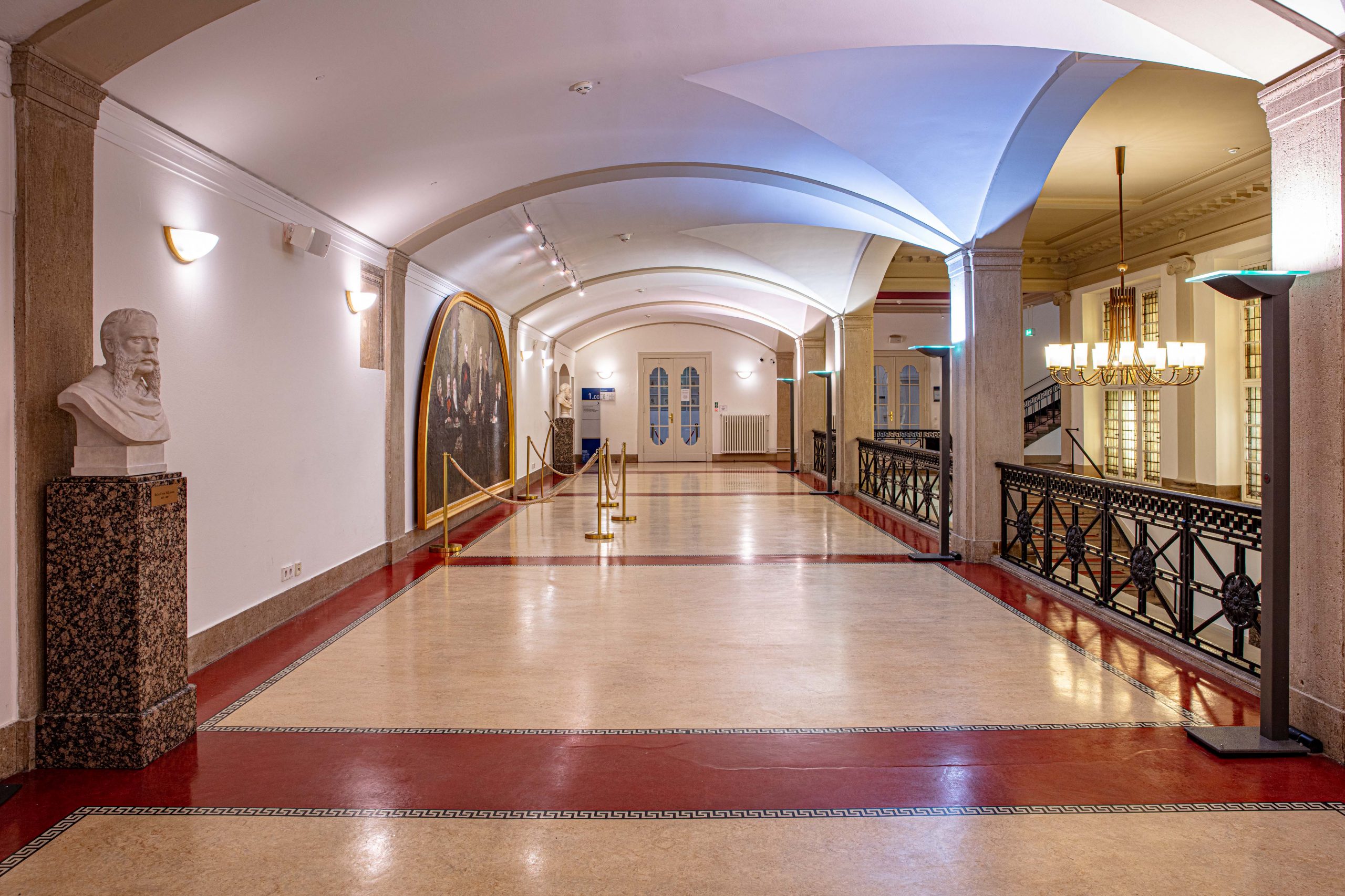 Historische Wandelhalle im LVH Langenbeck Virchow Haus Berlin mit roten Bodenflächen, Skulpturen und Blick auf den Eingangsbereich