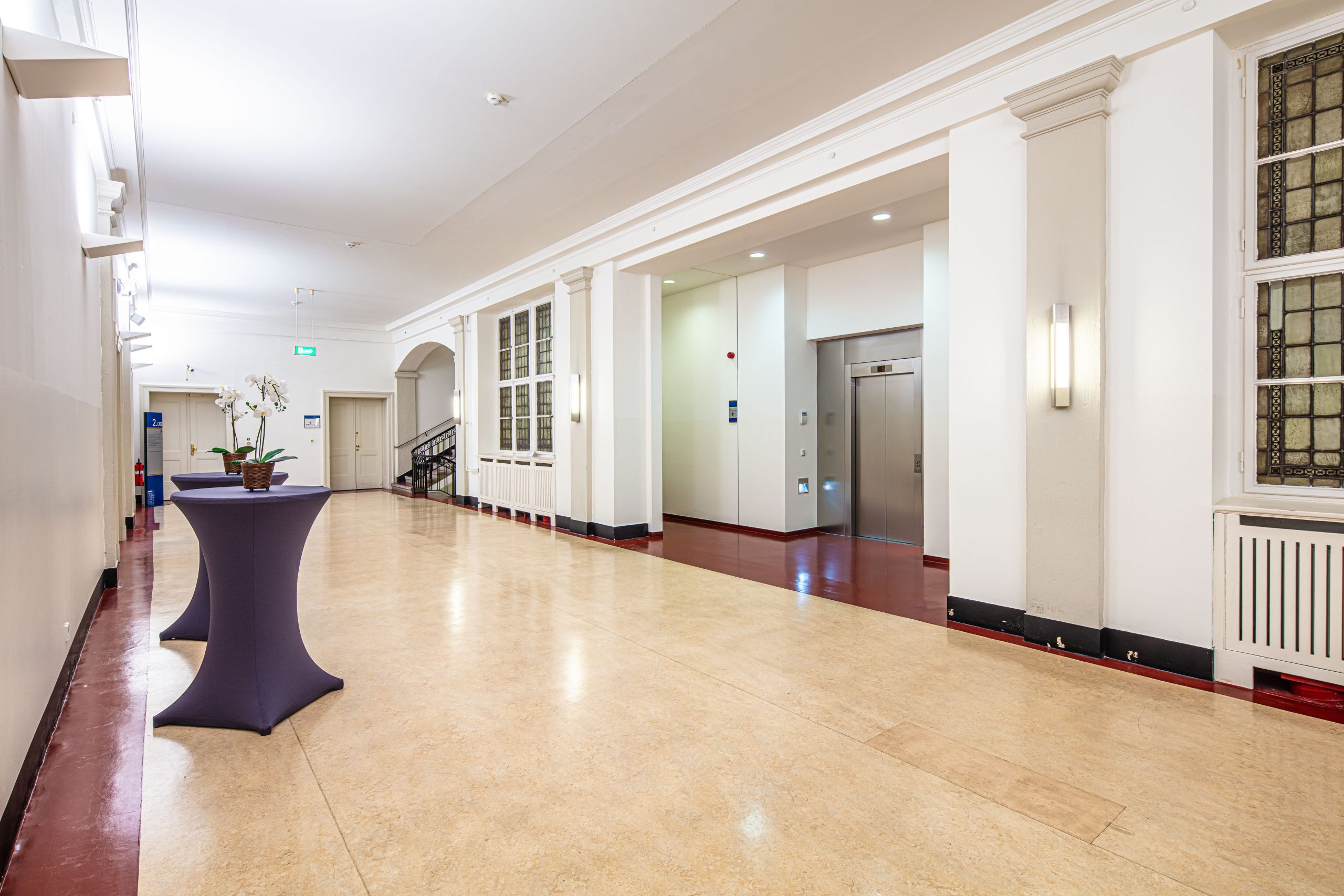 Foyer im 2. Obergeschoss des Langenbeck-Virchow-Hauses in Berlin mit Aufzug, Stehtischen und historischer Architektur.