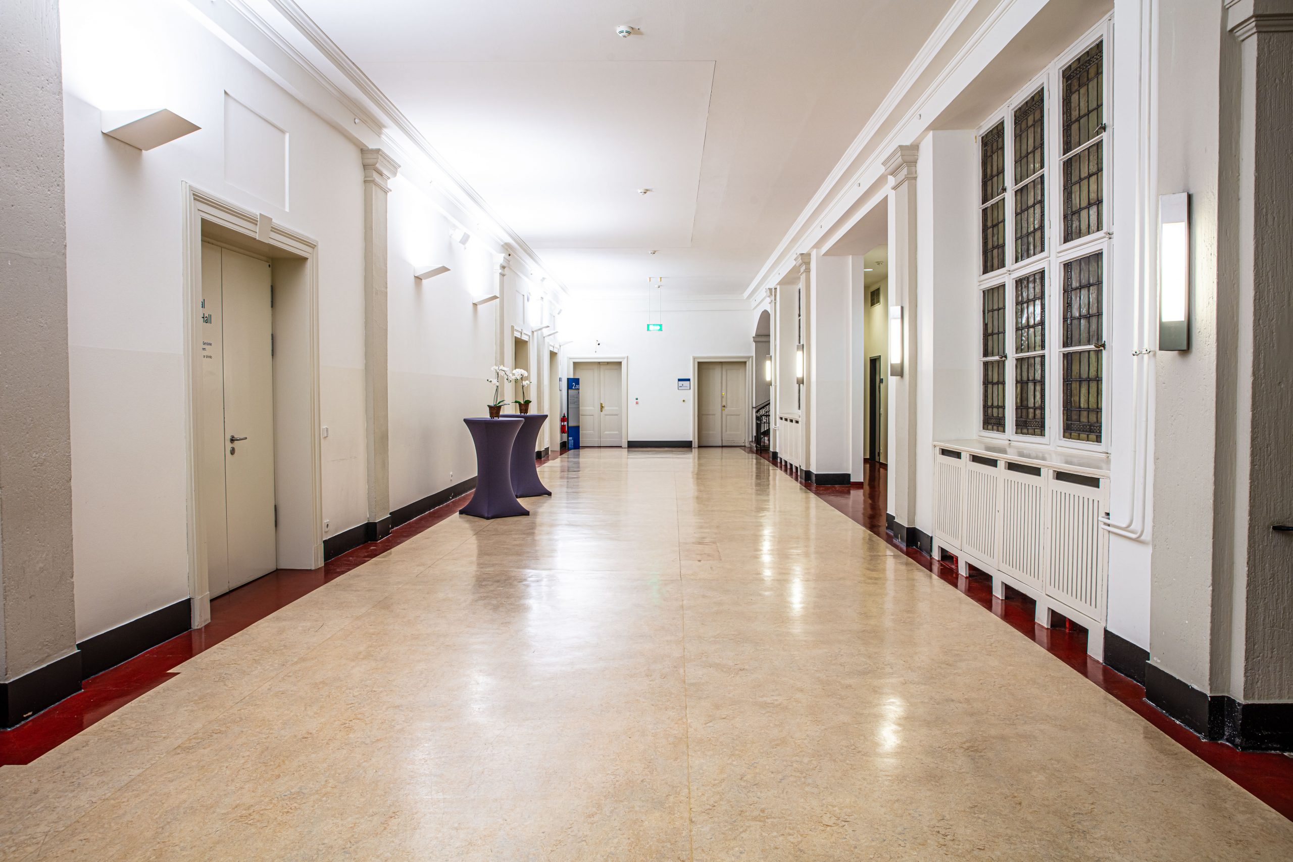 Blick in den hellen Flur des Foyers im 2. Obergeschoss des Langenbeck-Virchow-Hauses in Berlin mit Stehtischen und großen Fenstern.