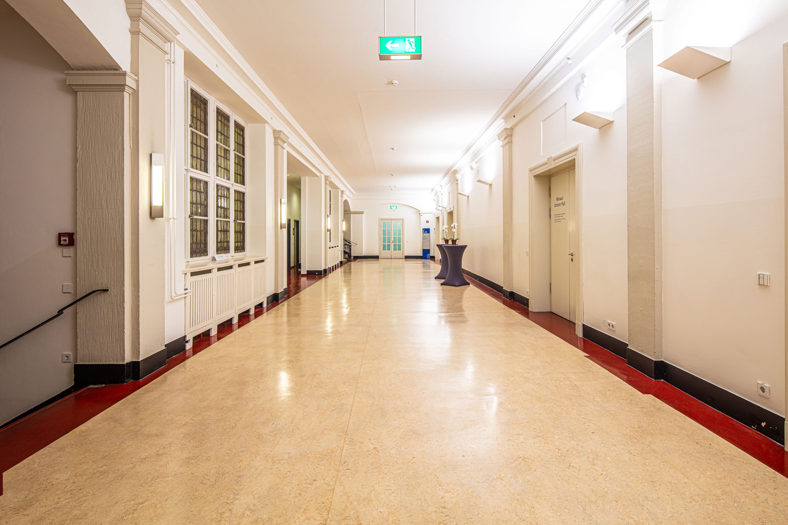 Blick in den hellen Flur des Foyers im 2. Obergeschoss des Langenbeck-Virchow-Hauses in Berlin mit Stehtischen und großen Fenstern.