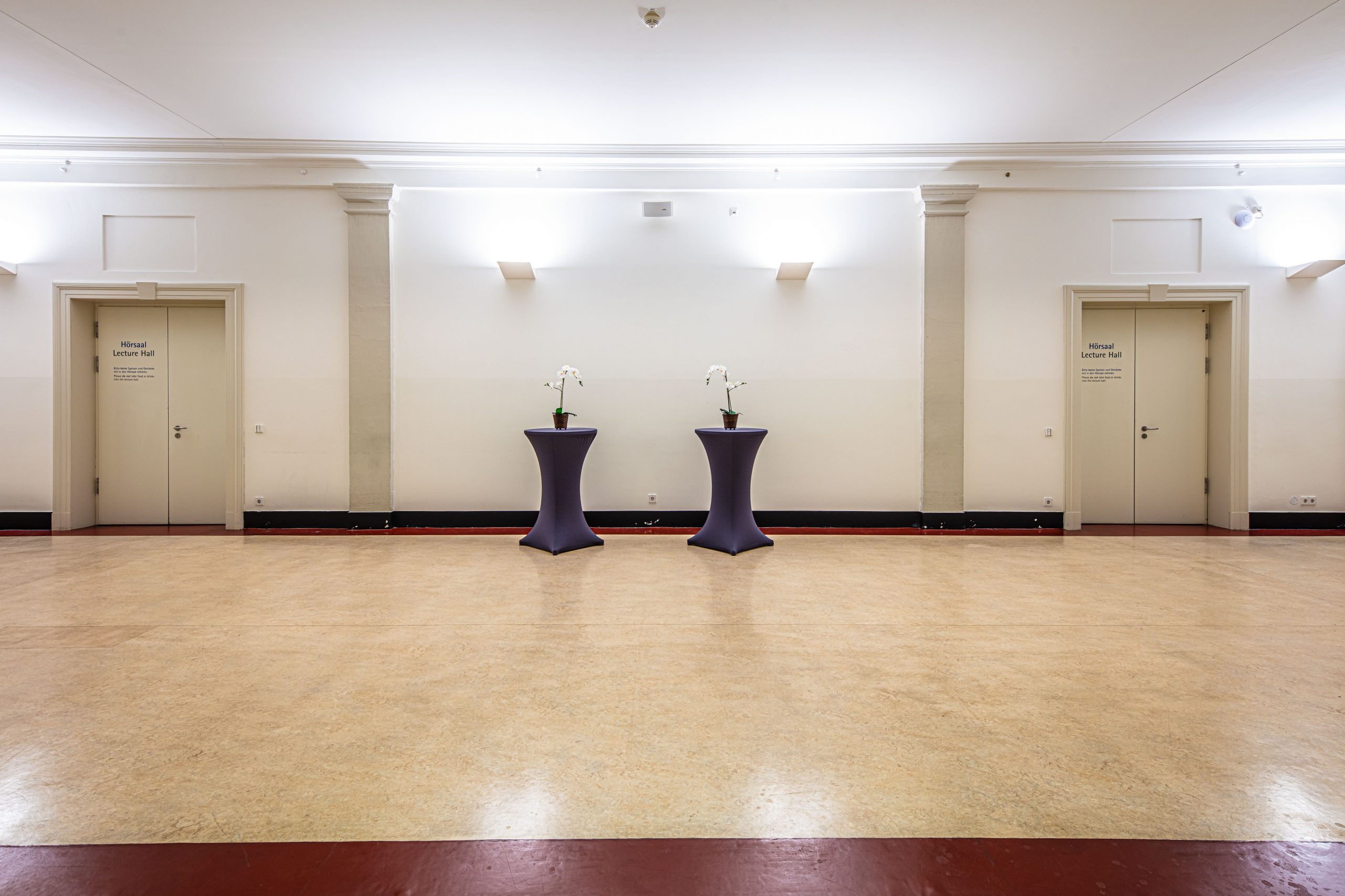 Foyer im 2. Obergeschoss des Langenbeck-Virchow-Hauses mit zwei Stehtischen in der Mitte, hellem Boden und schlichter Wandgestaltung. Ideal als Empfangs- und Pausenbereich bei Events.