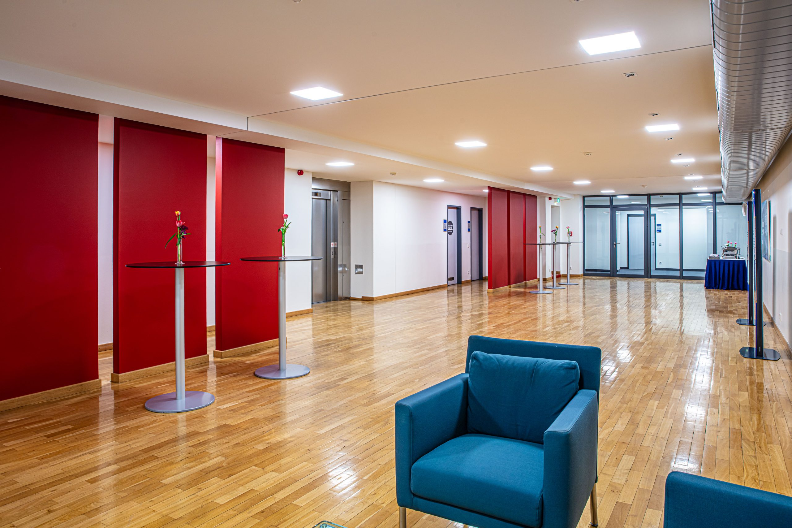 Foyer 4. Obergeschoss im Langenbeck-Virchow-Haus Berlin mit roter Wandgestaltung, Stehtischen und Sesseln auf hellem Parkettboden